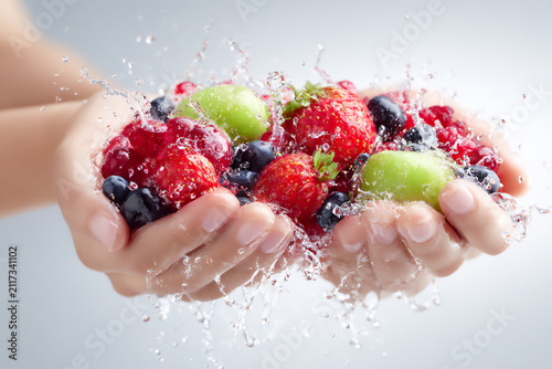 Hands hold a mix of fresh fruits with water splashing around in a bright setting