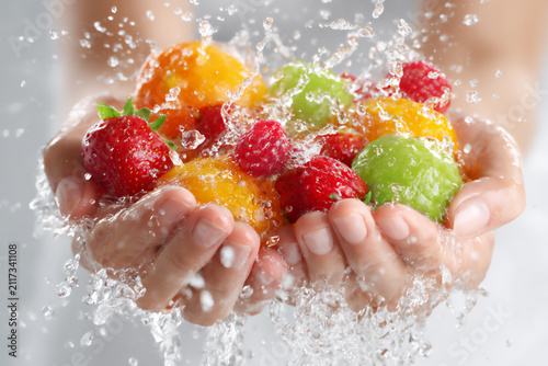 Hands holding mixed fruits with water splashing in a bright setting