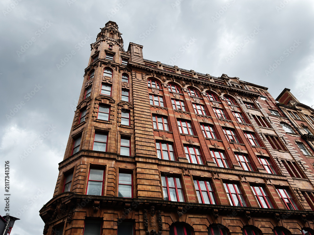 Obraz premium Historic red brick office building with ornate Victorian architecture in Manchester UK under dramatic cloudy sky