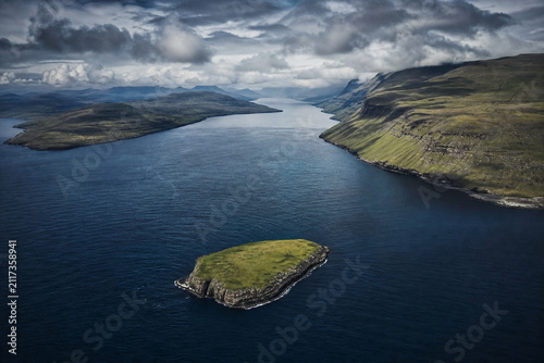 Aerial view of a small green island separated from mainland by a deep dark blue channel.