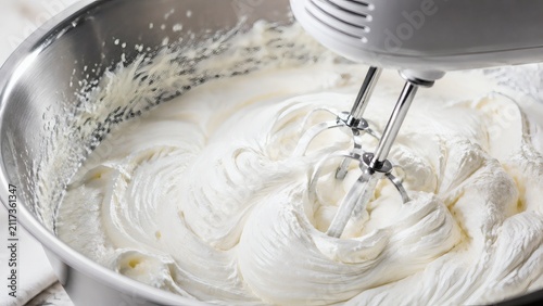 Whipped cream being mixed in a stainless steel bowl with mixer  
