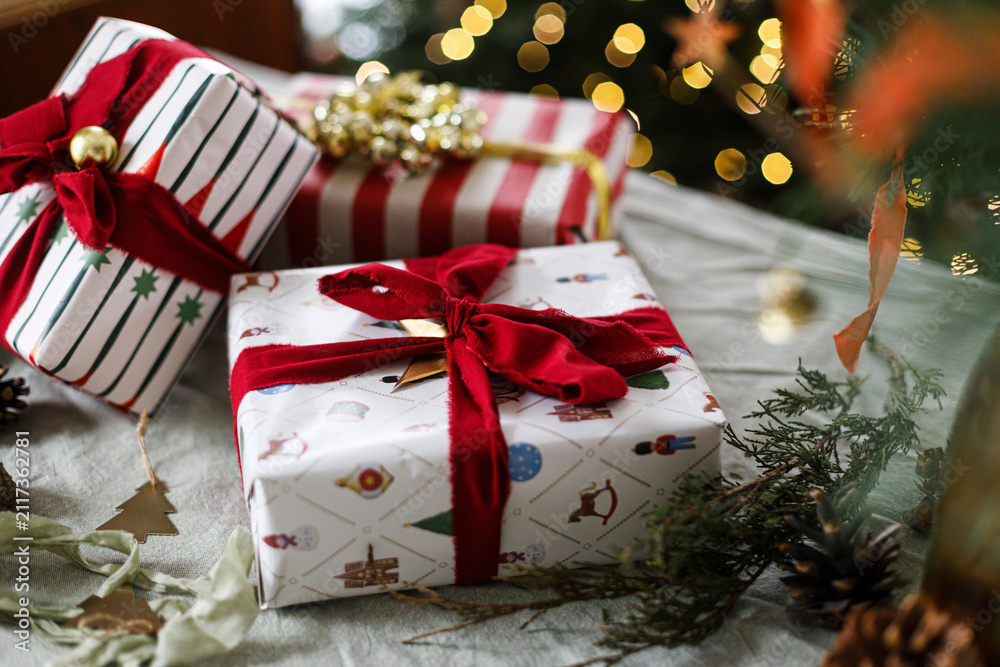 Obraz premium Merry Christmas! Stylish wrapped Christmas gift boxes on table on background with decorated xmas tree and warm glowing bokeh lights. Cozy winter holiday celebration, xmas eve atmosphere