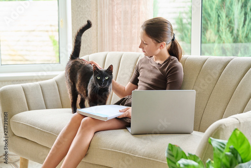 Friendship of a 10-year-old girl and her black cat sitting on sofa at home