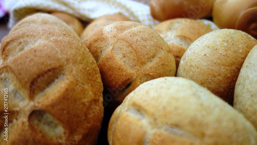 Freshly baked artisan bread rolls with a beautiful cross-shaped scoring on top. A close-up view of crusty bread loaves and rolls arranged on a rustic wooden surface, showcasing a variety of baked good