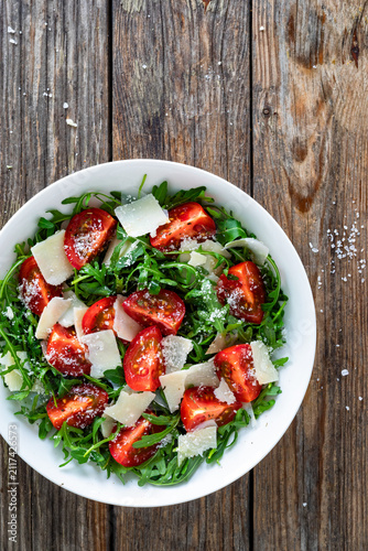 Arugula salad with tomatoes and parmesan cheese on wooden table

