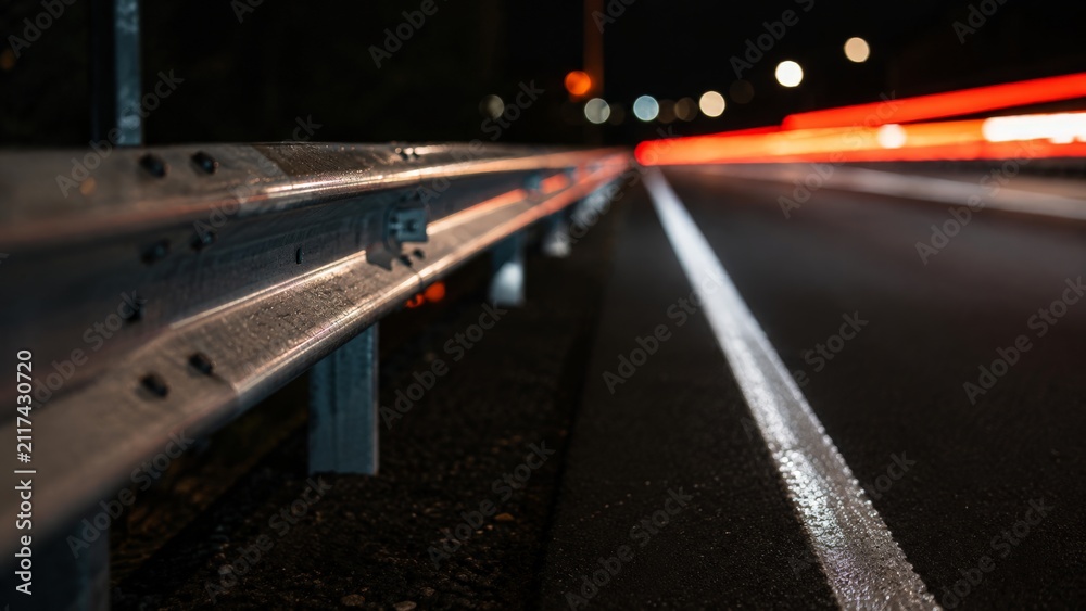 Fototapeta premium Highway guardrail with red car light trails at night.