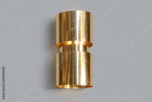 A cylindrical brass object with polished surfaces reflects light, highlighting its smooth, machine-made form against a neutral gray backdrop.