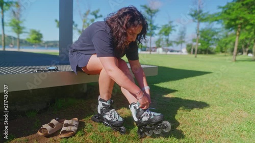 A Young Woman Prepares to Rollerblade on a Sunny Day, Adjusting Her Skate Gear While Sitting on a Green Lawn Under the Clear Blue Sky