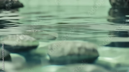 Close-up view of smooth river stones submerged beneath clear rippling water surface with soft green tones