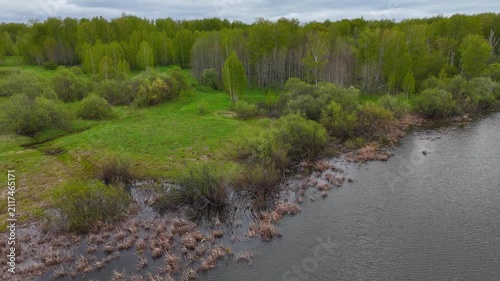 A panoramic view from above of the shores of a wide lake surrounded by forest on a cloudy summer day. Lake Bykovskoye, Novosibirsk Oblast, Russia.
