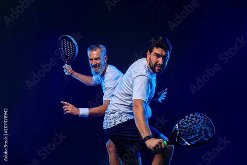 Padel tennis doubles. Two athletes players with racket. Man athlete with paddle racket on court with neon colors. Sport concept. Download a high quality photo for the design of a sports app
