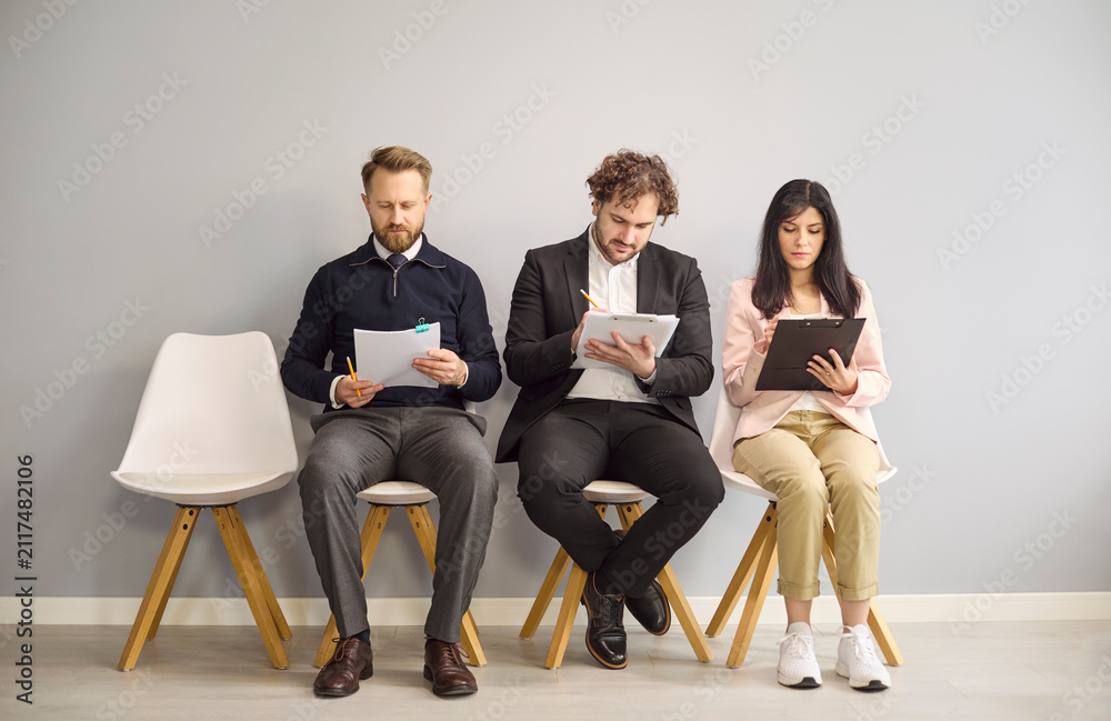 Obraz premium Candidates interview hiring recruitment applicants waiting with paperwork. Three business applicants fill resume and notes before assessment. Clear hiring recruitment and assessment concept.