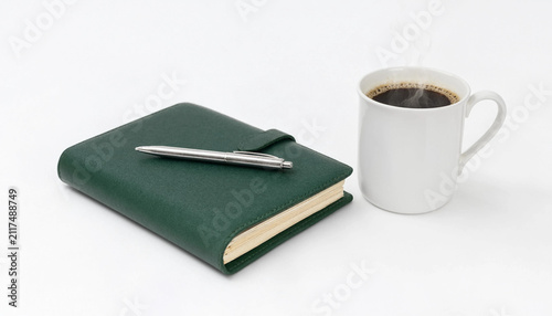 Green notebook with a silver pen and a cup of black coffee on a desk
