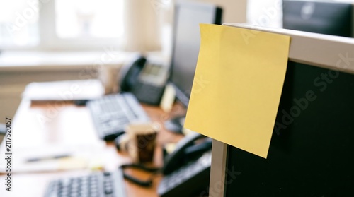 Blank yellow sticky note stuck on computer monitor in modern office workplace with copy space for message