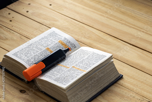 Open English dictionary book with orange highlighter marker pen highlighting important vocabulary words and definitions on a rustic wooden plank table, learning and education concept for students