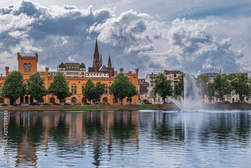 The Pfaffenteich, located in the heart of Schwerin, features a fountain and the former Grand Ducal Administrative Building on the opposite side of the pond.