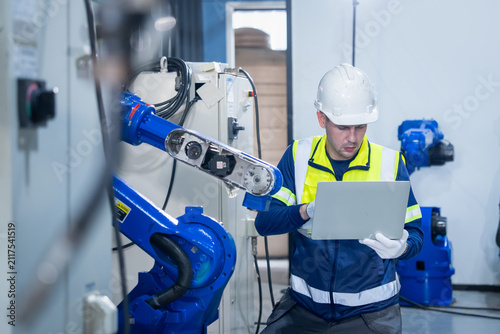 Canvas Print Industrial technician operating a laptop to oversee a robotic arm in a modern sm