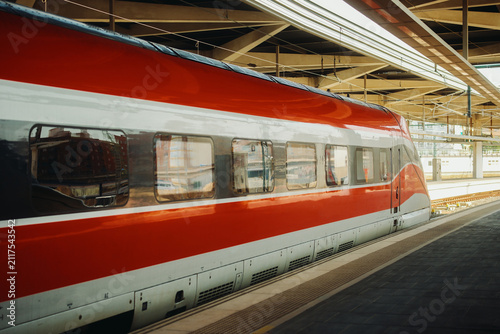 Fotografie Modern red and white high speed train standing at a covered railway station platform