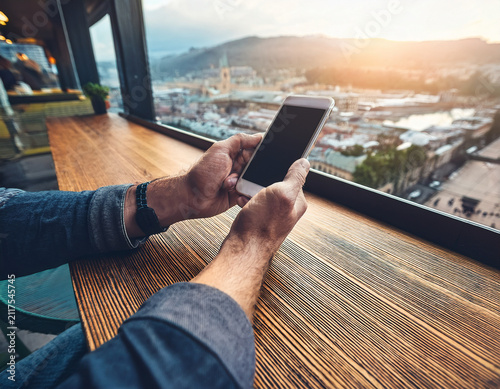 Hands Using Smartphone at Outdoor Cafe With Scenic Urban Background View