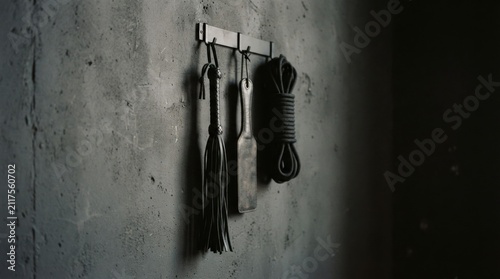 Black leather whip paddle and rope hanging on wall