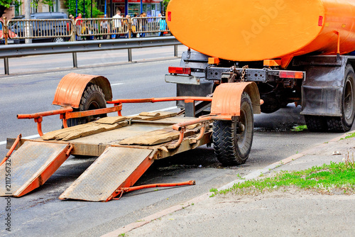 Truck with trailer parked on roadside during daytime near busy street.