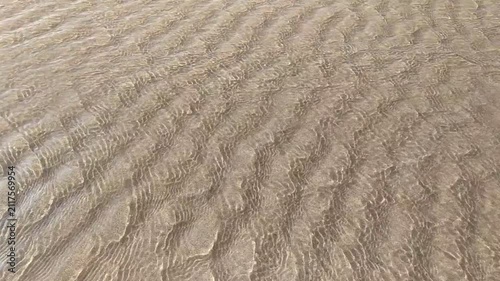 Crystal clear water ripples over a textured sandy beach, evoking tranquility and natural peace. This highangle shot, featuring no people, captures the serene beauty of the coast for backgrounds.
