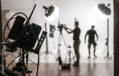 Silhouetted figures of a film crew working under professional studio lighting with camera equipment. Concept of filmmaking, media production, and backstage work environments.