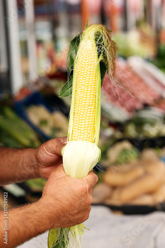 Male seller recommending fresh sweet corn at outdoor farmers market. Local agriculture business, organic crop retail, and fresh grocery trade concept.