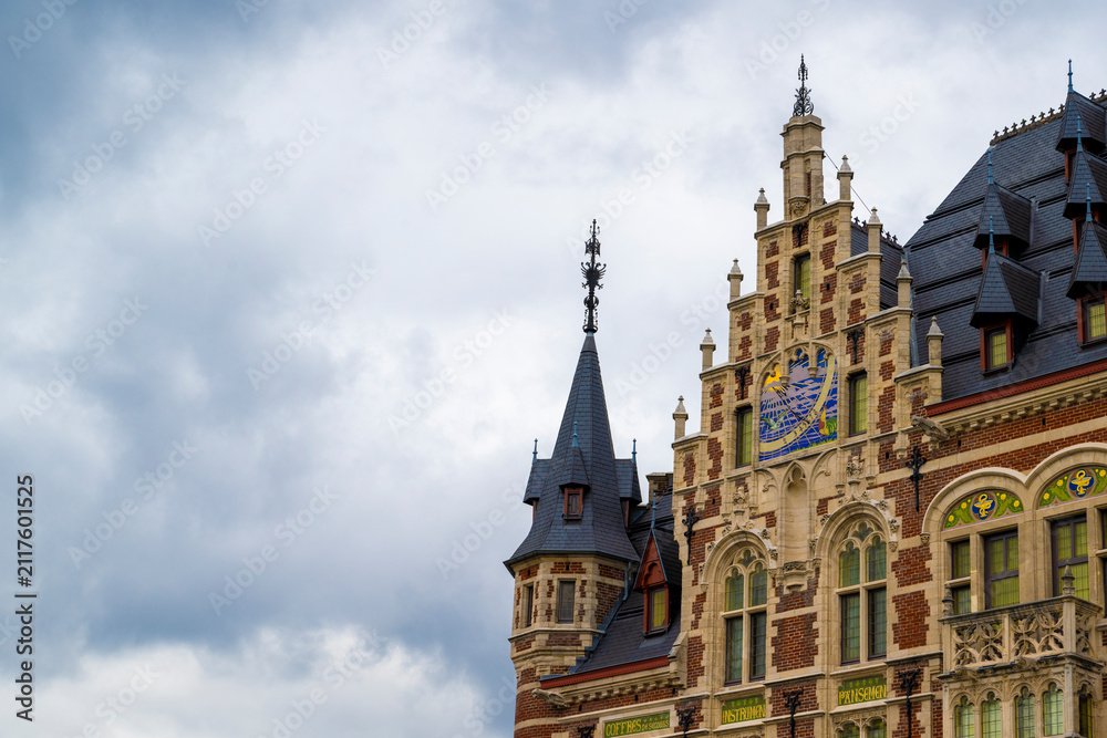 Fototapeta premium Historic European civic building with decorative tower and colorful clock standing beneath expansive cloudy sky providing generous copy space for design