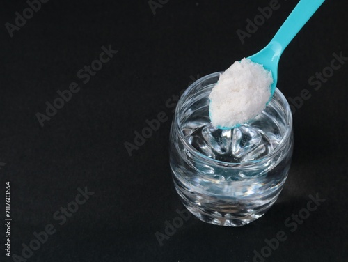 Foto A glass of saltwater solution with blue spoon filled with sea salt crystals on a