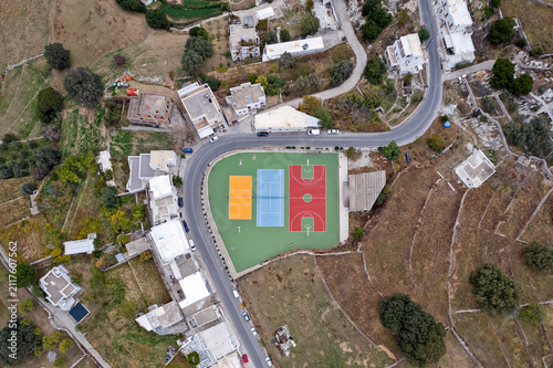 Aerial view of a colorful sports court in Apeiranthos village, Naxos island, Greece, surrounded by winding roads, white houses, terraced fields and the rural cycladic landscape.