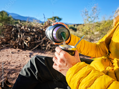 Close up of woman pouring hot water from thermos into mate cup outdoors in nature