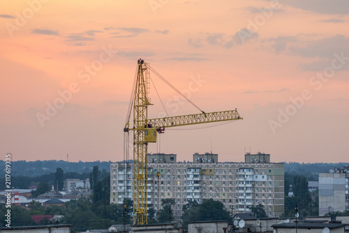 A tower crane towers over residential high-rise buildings against a cloudy evening sky during urban construction