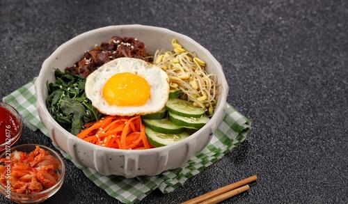Bibimbap is a Korean dish in the form of a bowl of white rice topped with side dishes of vegetables, beef, eggs and spicy gochujang sauce.