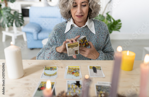 Senior woman reading tarot cards on table at home