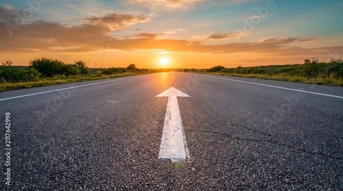 Business strategy and future roadmap concept depicted by a directional white arrow on an empty highway pointing towards a glowing sunset horizon