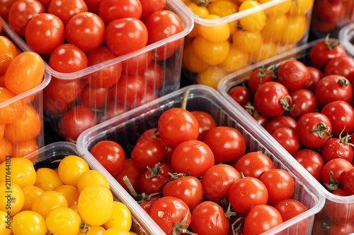 Fotografie Assorted fresh red, orange, and yellow cherry tomatoes packaged in clear plastic containers for sale at a local farm market