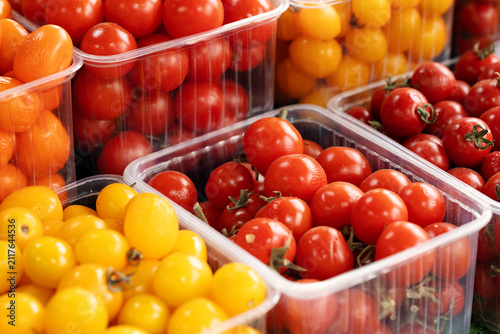Assorted fresh red, orange, and yellow cherry tomatoes packaged in clear plastic containers for sale at a local farm market. Concept of organic produce and food retail.