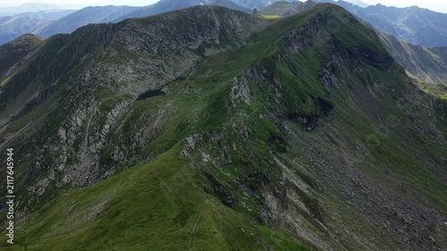 Drone flying backward above a mountain hiking trail revealing a remote alpine lake surrounded by dramatic peaks in Romania's Făgăraș Mountains.