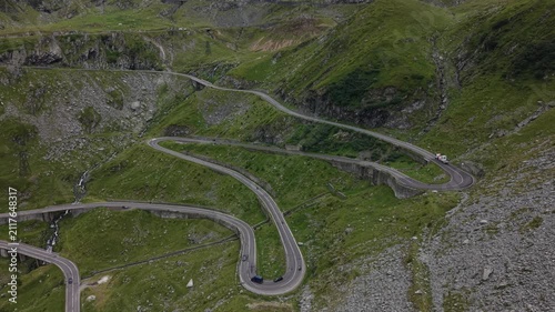 Wide static drone view showing multiple Transfăgărășan hairpin bends with continuous vehicle traffic crossing Romania's spectacular alpine landscape.