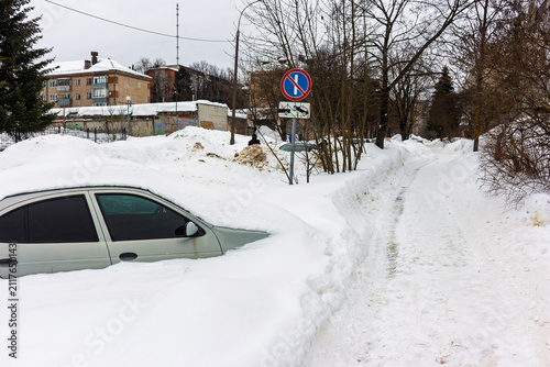 Fotografie Silver sedan engulfed by towering snowdrifts after a harsh winter blizzard, parked on an urban street