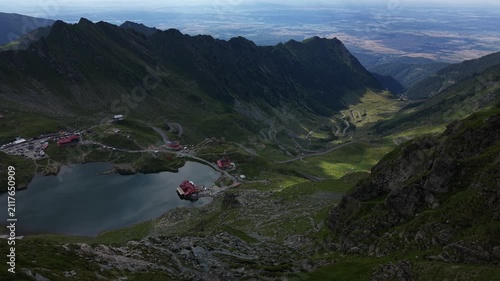Static aerial view overlooking Bâlea Lake with vehicles traveling along the Transfăgărășan road while hikers explore the surrounding mountain landscape.