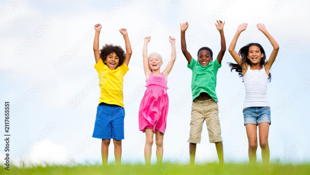 Fototapeta premium Four children jumping with arms raised on grass, showing joy and energy with a bright sky background. Suitable for family, education, and health themes with copy space.