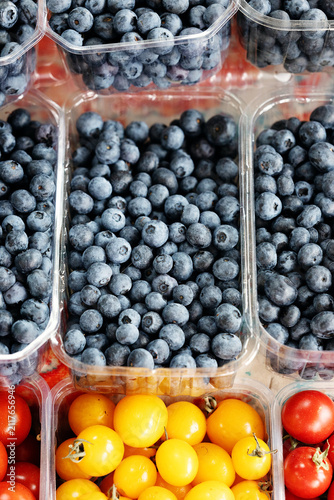 фотографія Plastic punnets filled with fresh unwashed blueberries and colorful cherry tomatoes on display at a farm market
