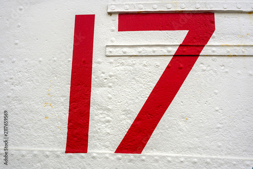 Bold red number 17 painted on a weathered white metal panel with visible rivets and texture