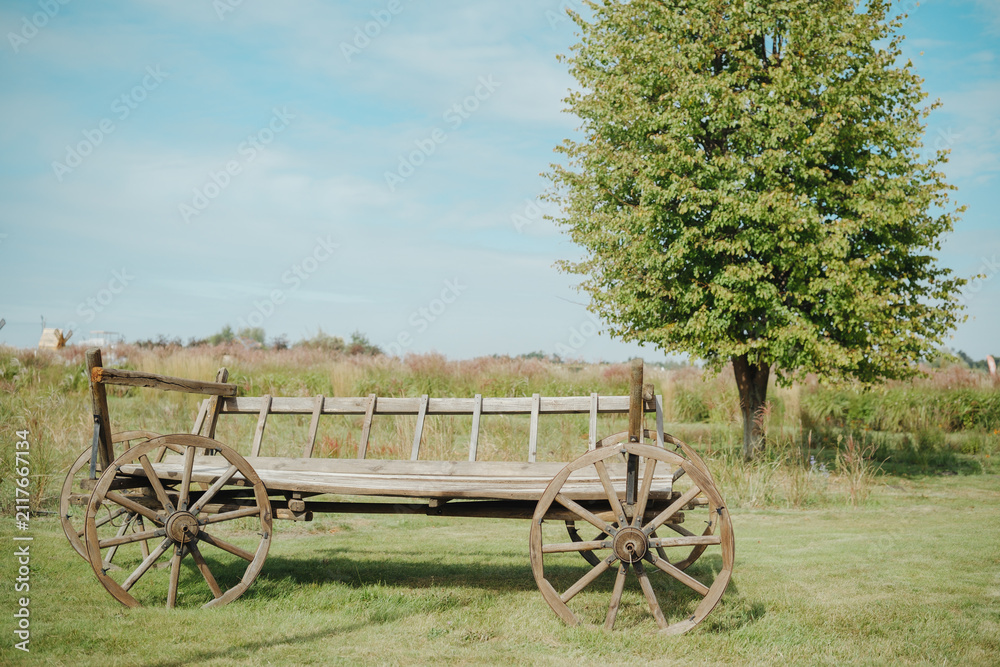 Obraz premium Old wooden cart with large wheels in green field under blue sky