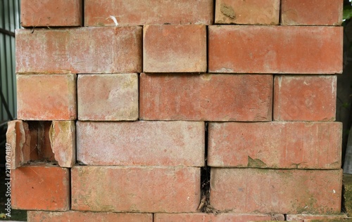A stack of red bricks without mortar. The blocks are unevenly laid, with shifts and gaps. The clay texture is uneven, with chips, scratches, and abrasions on the weathered surface.