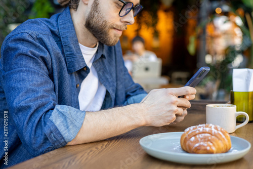 Foto Bearded young caucasian man with a phone in a cafe