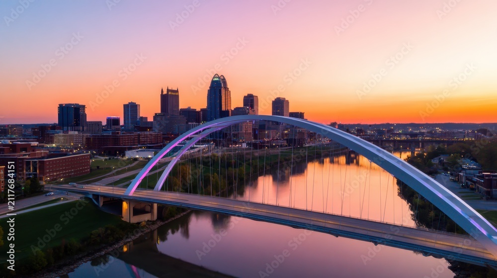 Obraz premium A vibrant city skyline under a stunning sunset with a reflecting river and modern arch bridge