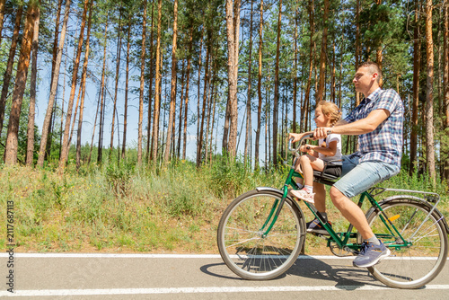 Young father with his little daughter on bicycle in summer sunny forest